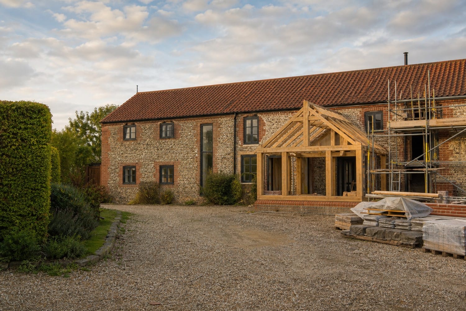 Norfolk flint barn conversion with an oak-framed extension under construction at sunset