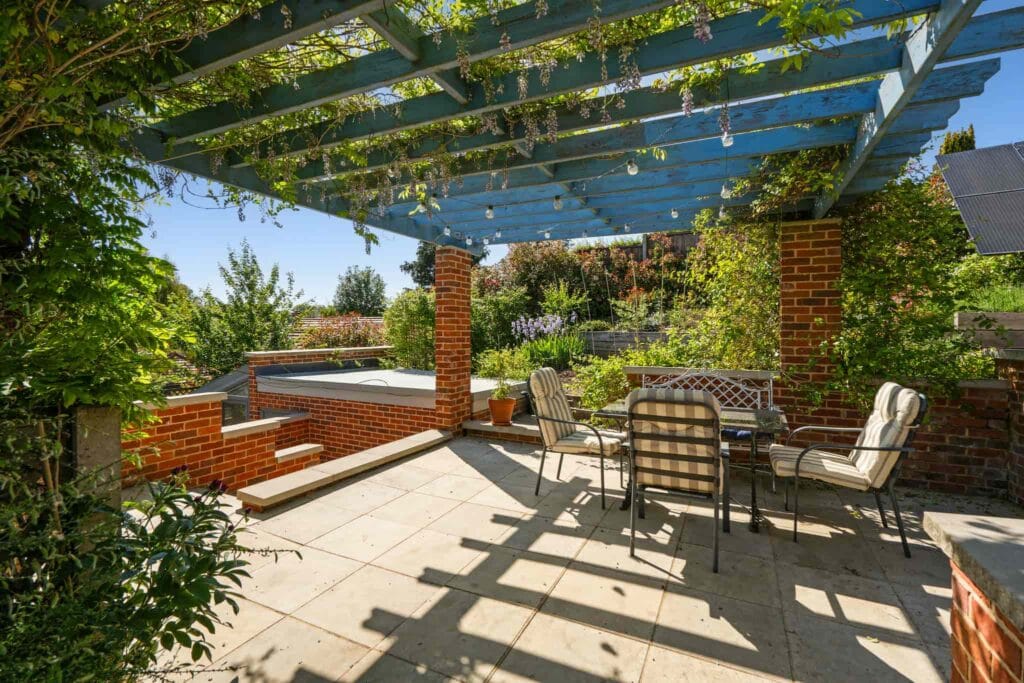 Sunlit pergola with wisteria above a tranquil garden seating area.