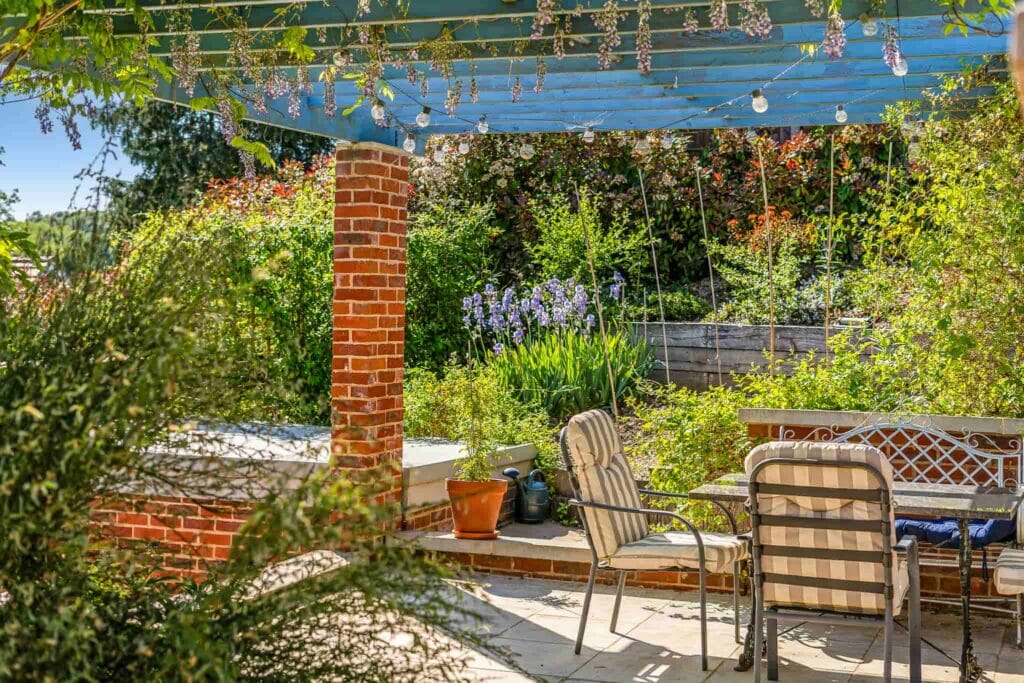 Shaded garden terrace under wisteria pergola.
