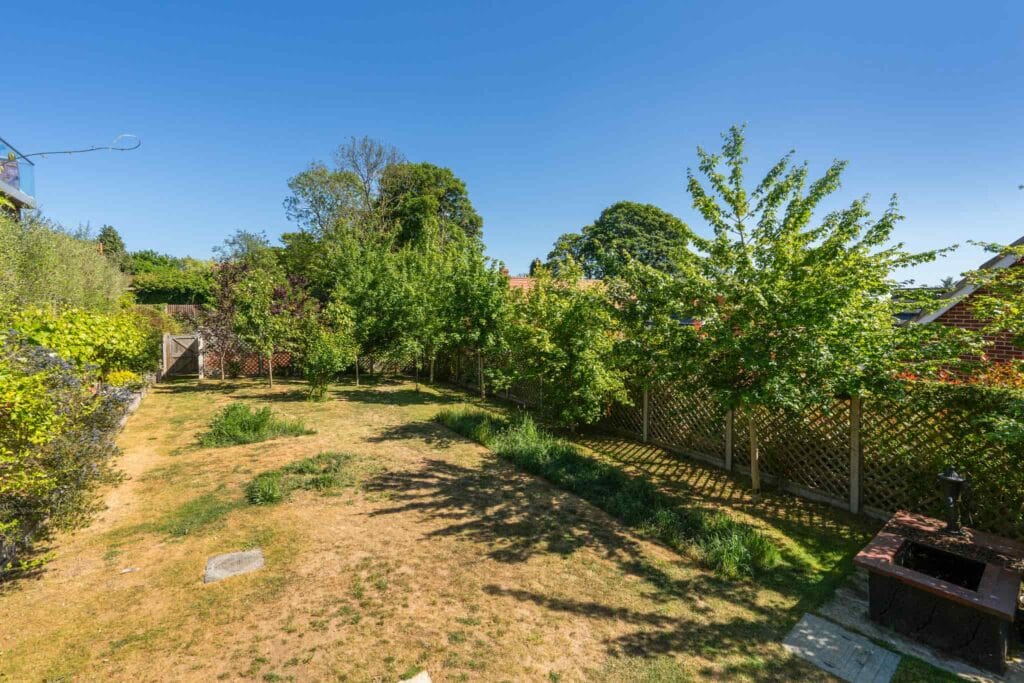Expansive lawn bordered by mature trees and lattice fencing.