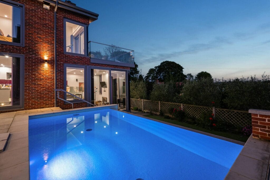 Illuminated infinity-edge pool beside the house, glowing beautifully under the evening sky.