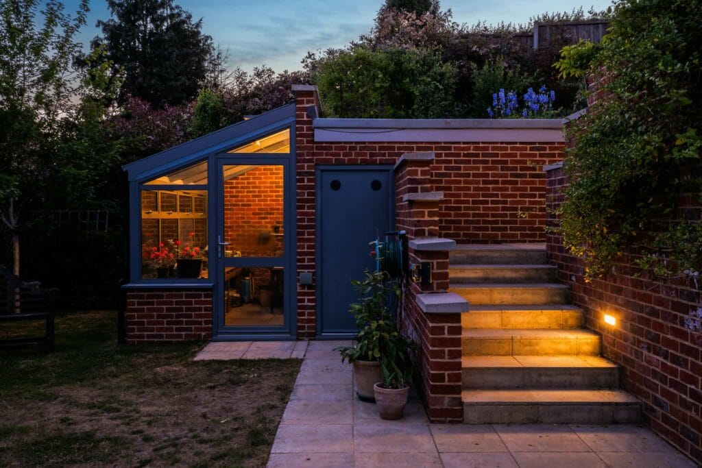 Charming brick greenhouse and garden steps softly lit at dusk.