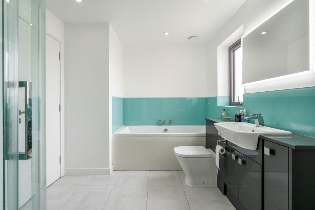 Guest ensuite with bath, walk-in shower, and sleek turquoise finishes.