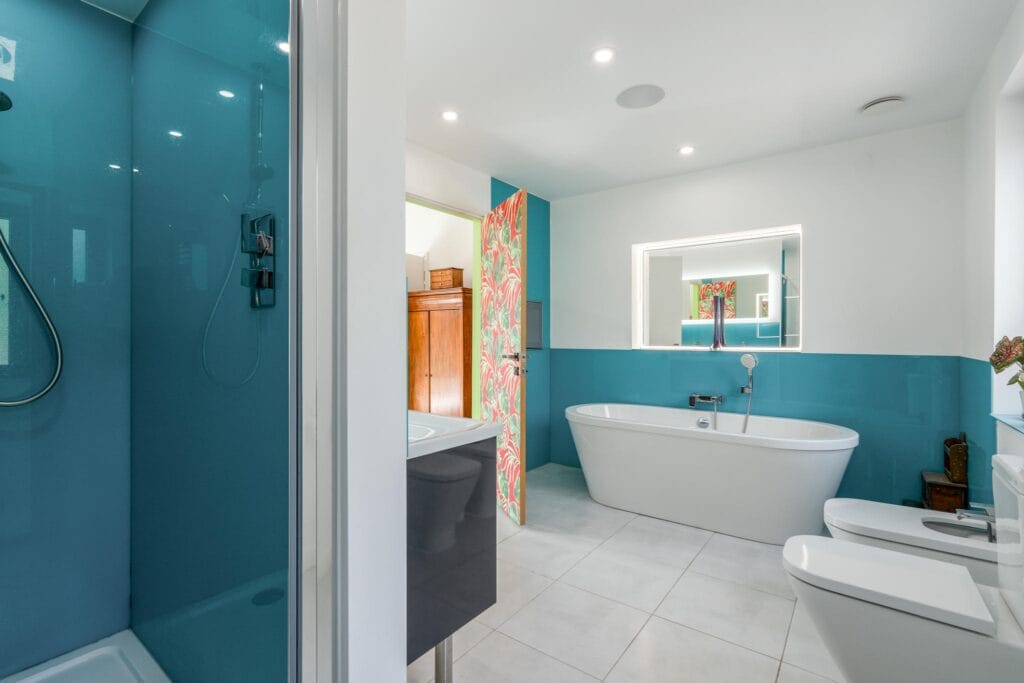 Principal ensuite with walk-in shower, freestanding tub, turquoise accents, and built-in bath TV.