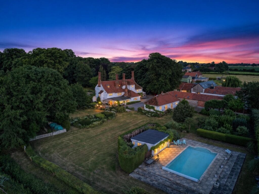 Sunset aerial view of estate with illuminated pool and vibrant sky