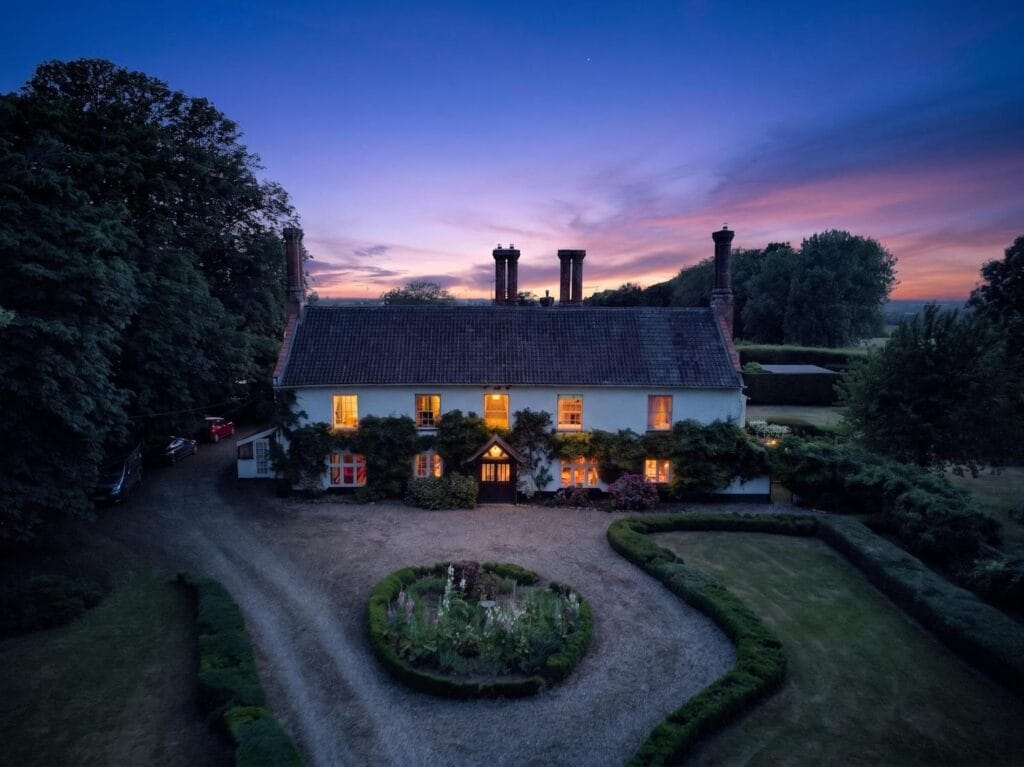 Twilight aerial view of country house lit up at dusk with purple sky
