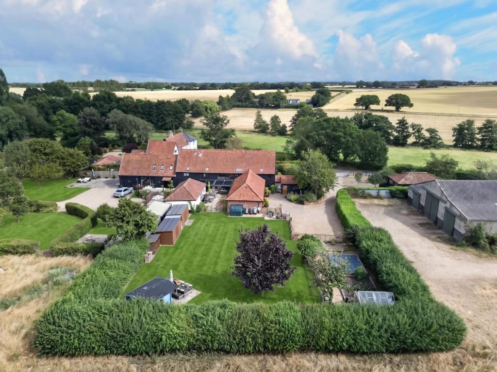 Aerial view of The Tithe Barn Sisland showing red-tiled barn complex, lawned grounds, hedged boundaries, and open Norfolk farmland beyond