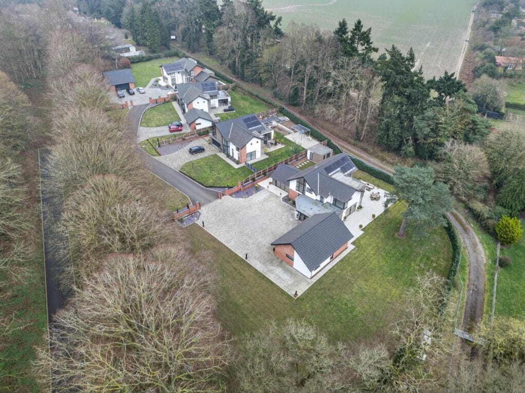 Aerial drone view of modern luxury homes in a private woodland development with large gardens and countryside surroundings.