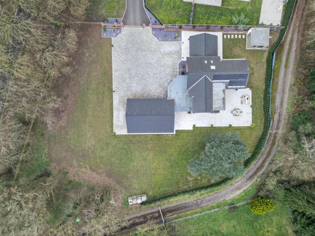 Top-down aerial drone view of a modern luxury home showing large driveway, detached garage, patio terrace and surrounding private garden.