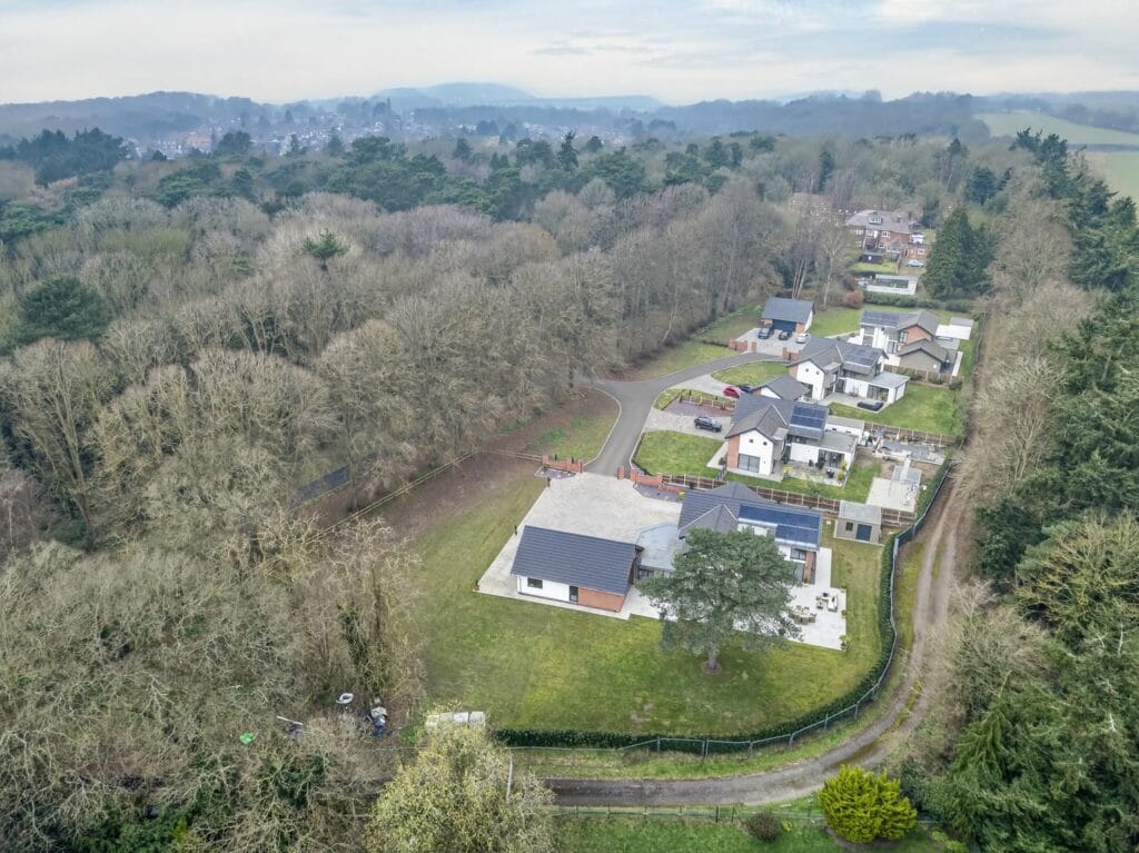 Aerial drone view showing a modern luxury home within a private woodland setting and surrounding countryside.