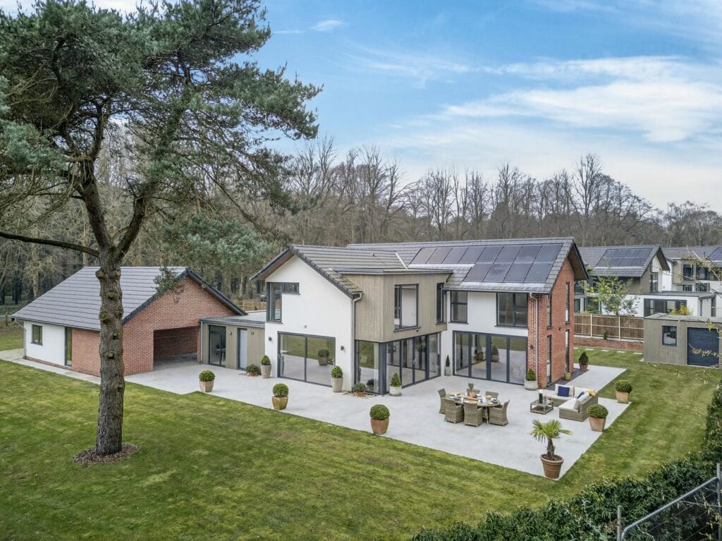 Elevated view of a modern architect-designed luxury home with large patio terrace, landscaped garden and detached double garage.