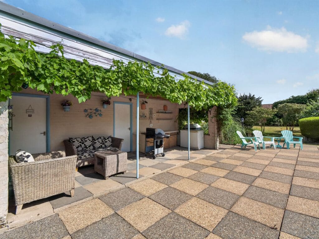 Vine-covered pergola terrace with rattan seating and outdoor kitchen