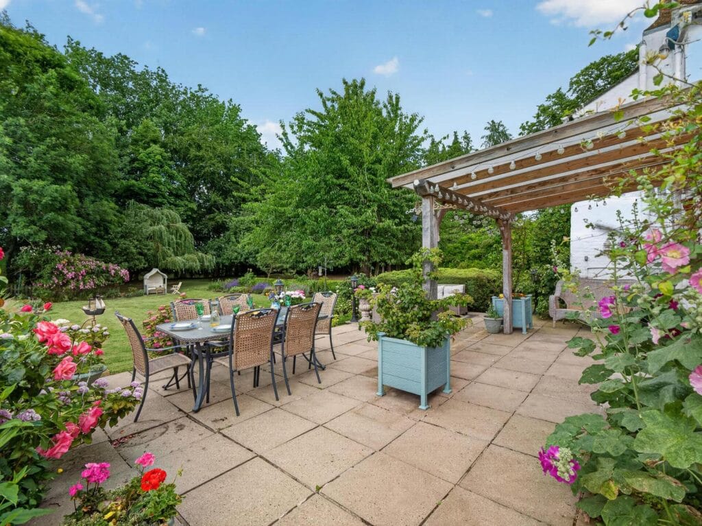 Stone patio with dining furniture and rose borders by pergola
