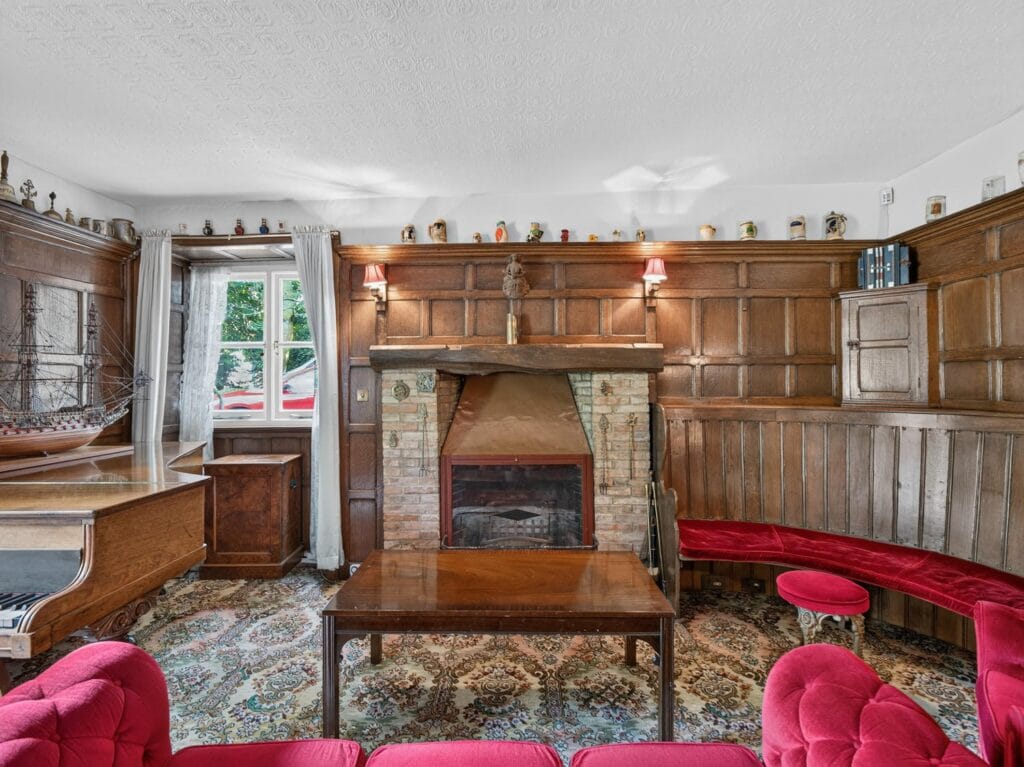 Oak-panelled sitting room with brick fireplace and red sofas