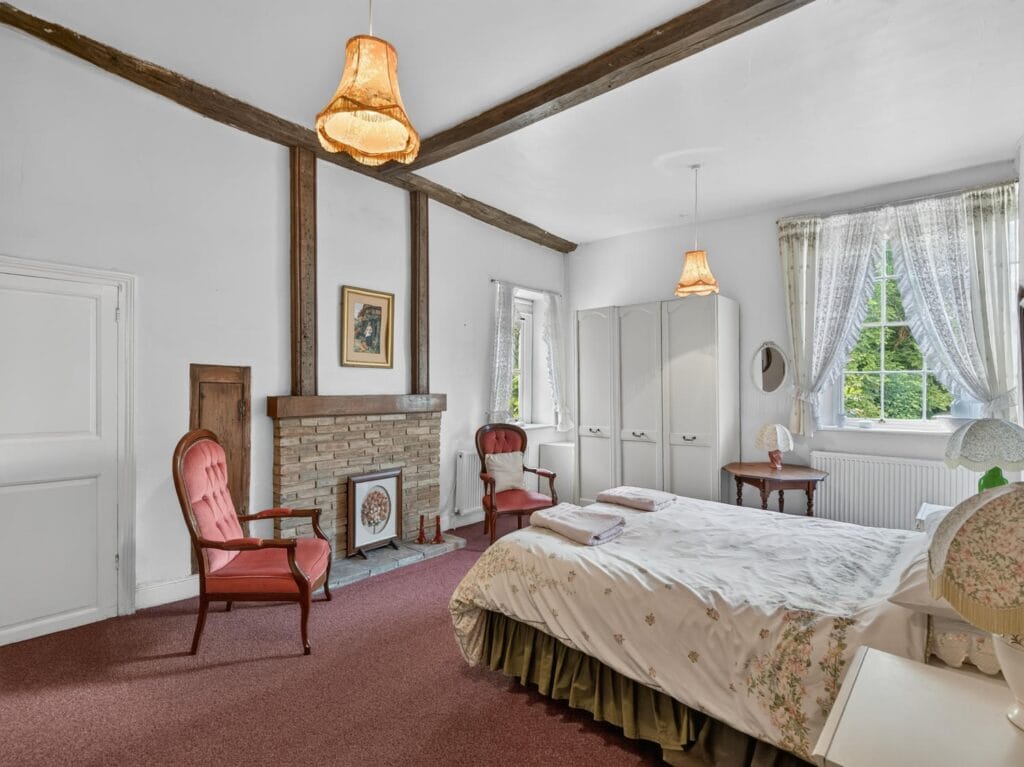 bedroom with exposed beams, stone fireplace and garden views
