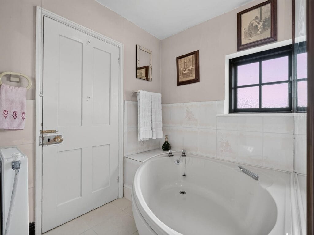 Bathroom with large corner bath and white tiled surround