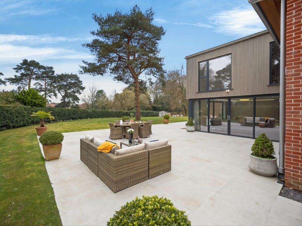 Modern luxury home patio with outdoor lounge seating and dining area overlooking a large private landscaped garden.