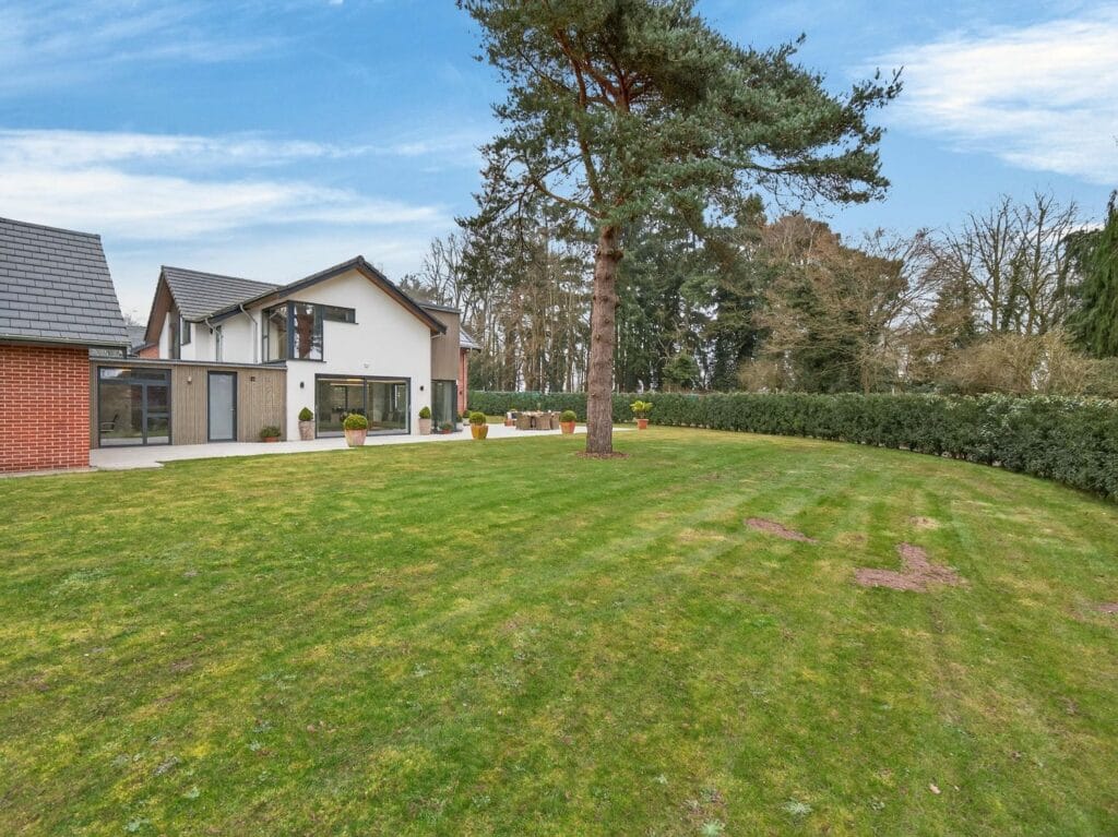 Large landscaped garden with mature trees and lawn behind the contemporary luxury home.