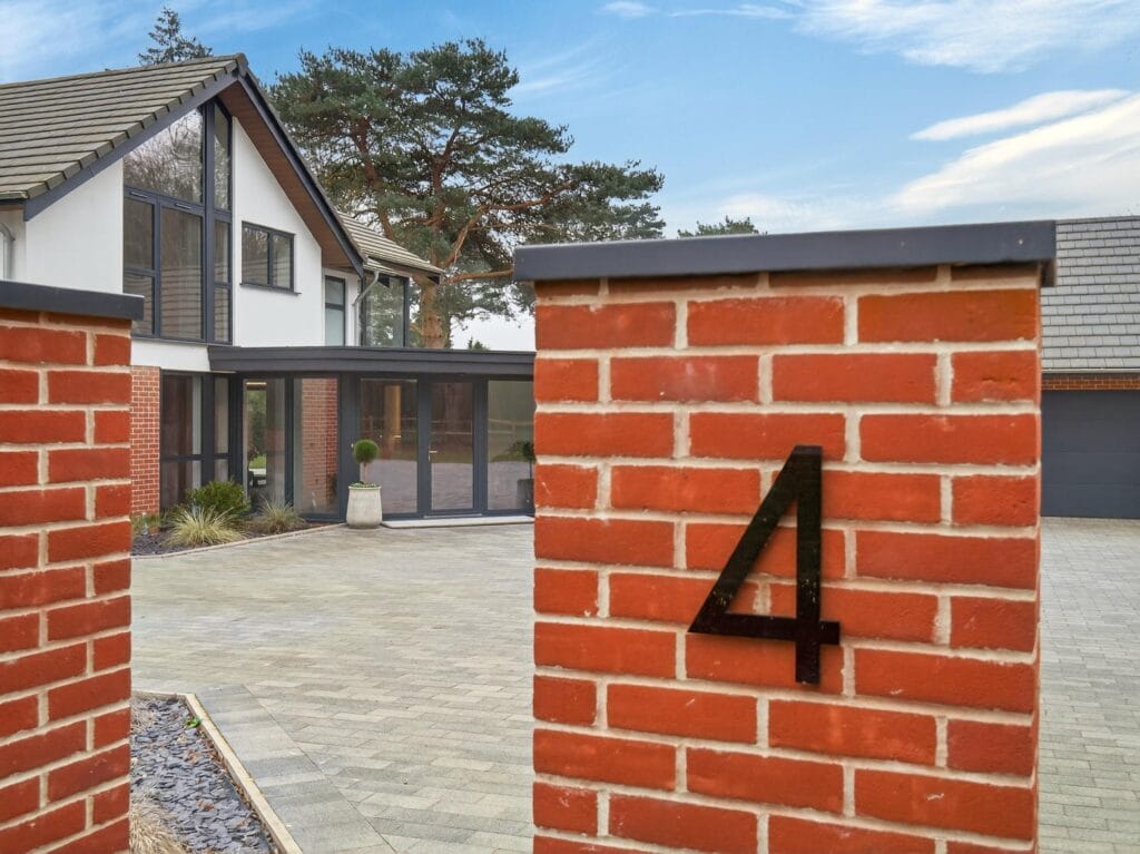 Luxury detached contemporary home entrance with brick gate pillars, large block paved driveway and modern architecture.