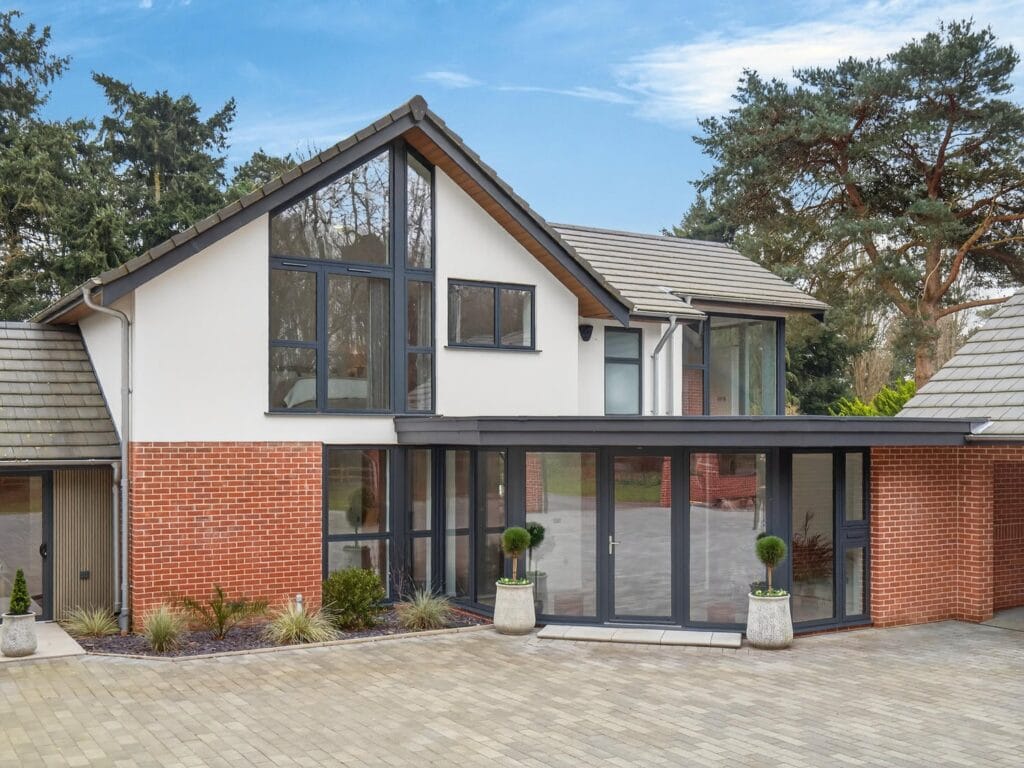 Luxury contemporary detached house with floor-to-ceiling glazing, modern entrance and large block paved driveway.