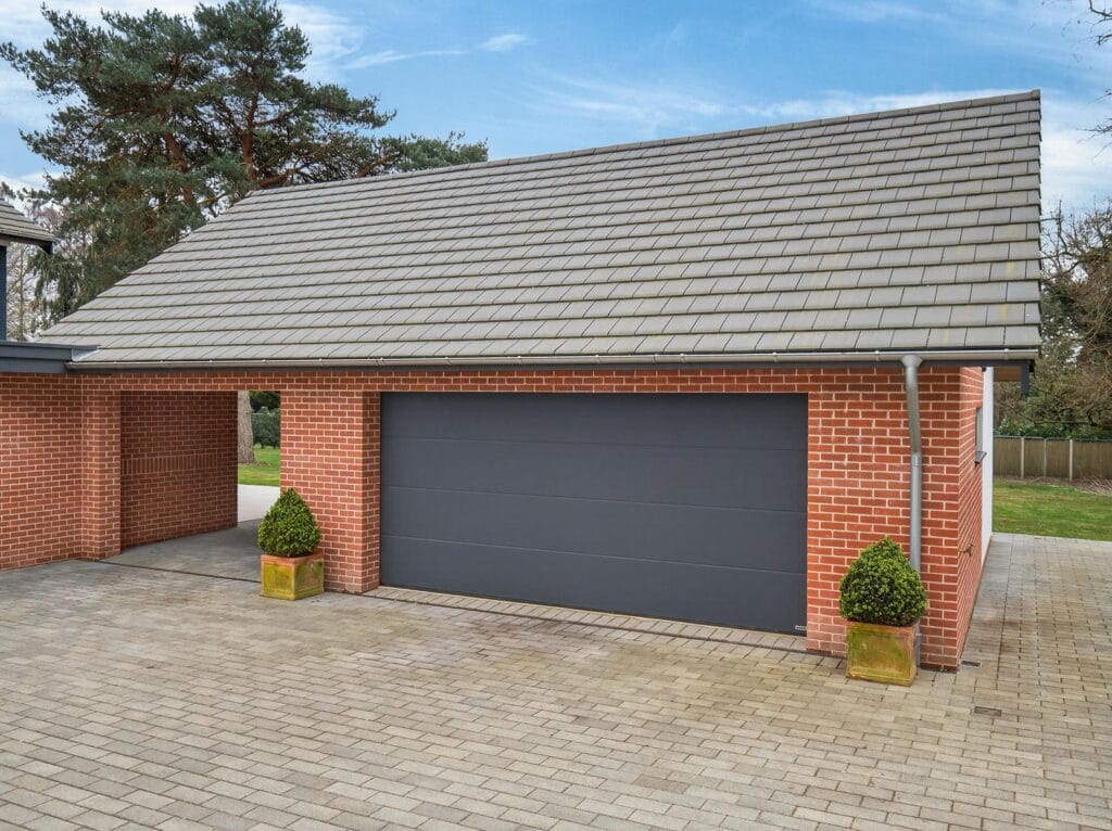 Detached double garage with electric door and covered access beside the block-paved driveway.