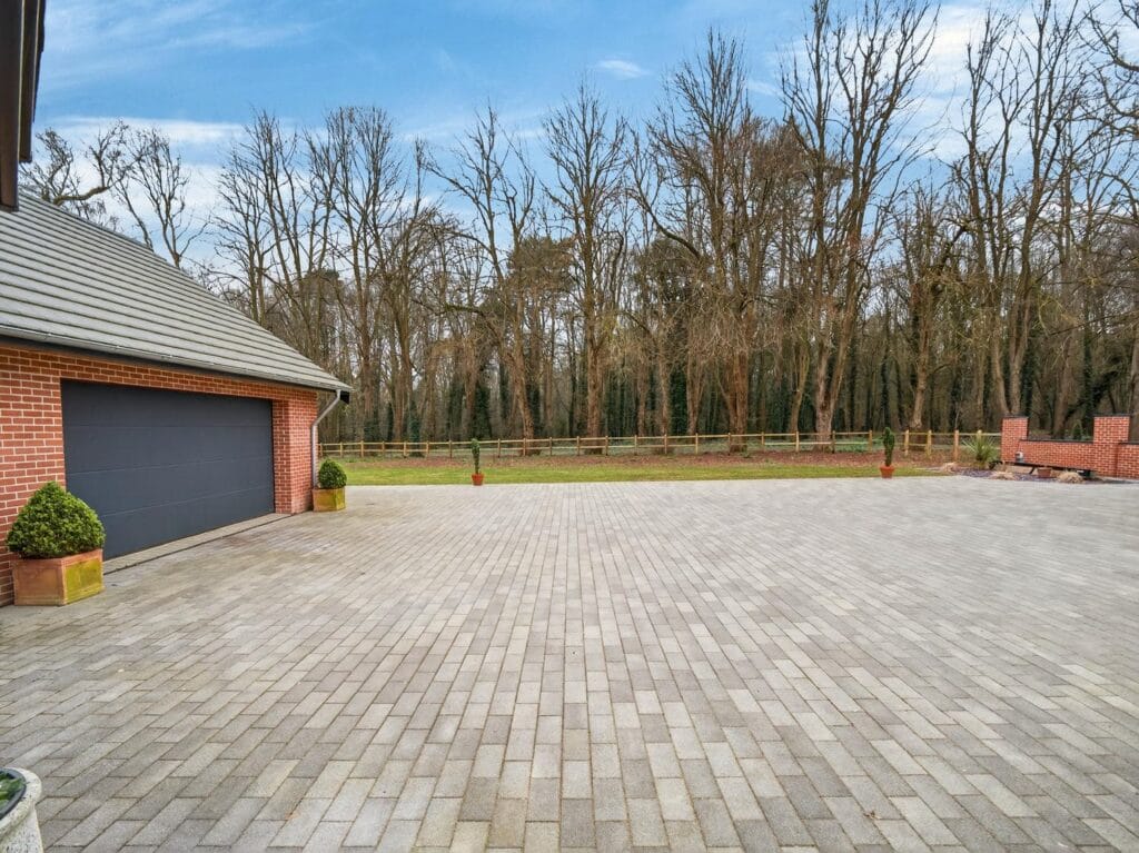 Large block-paved driveway with detached double garage and mature woodland backdrop.