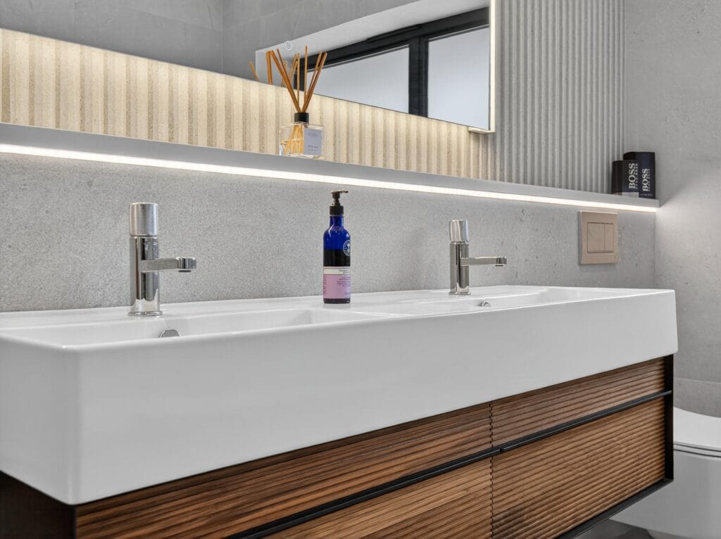 Contemporary double vanity basin with modern chrome taps, illuminated mirror and textured wall finish.