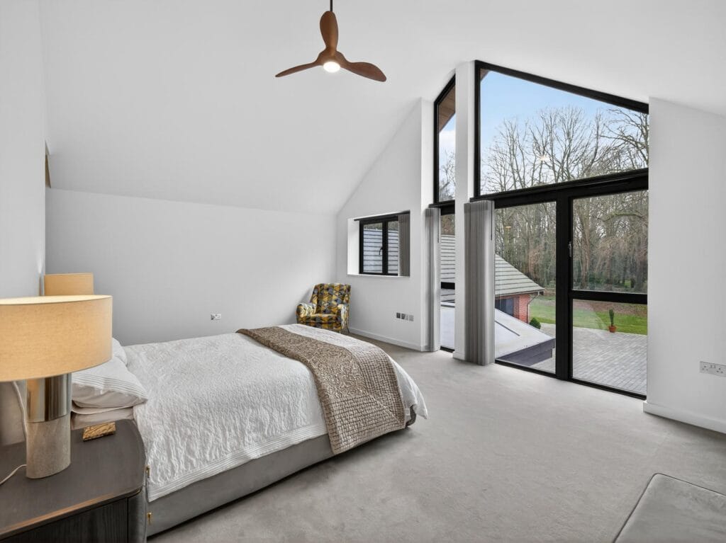 Luxury principal bedroom with vaulted ceiling, floor-to-ceiling glazing overlooking the garden.