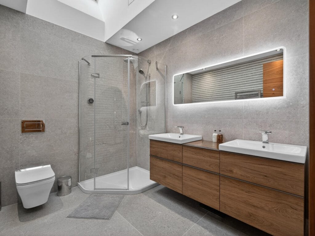 Modern ensuite bathroom with walk-in shower, double vanity unit, illuminated mirror and contemporary tiling.