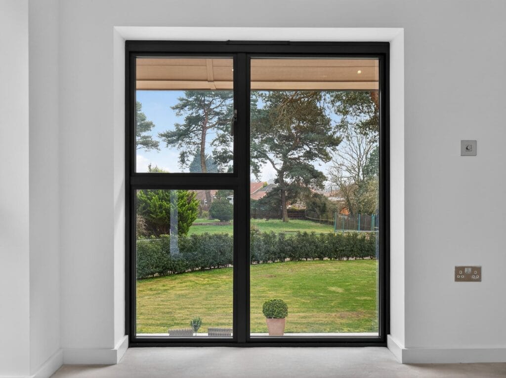 Large modern window with views across the landscaped garden and mature trees beyond.