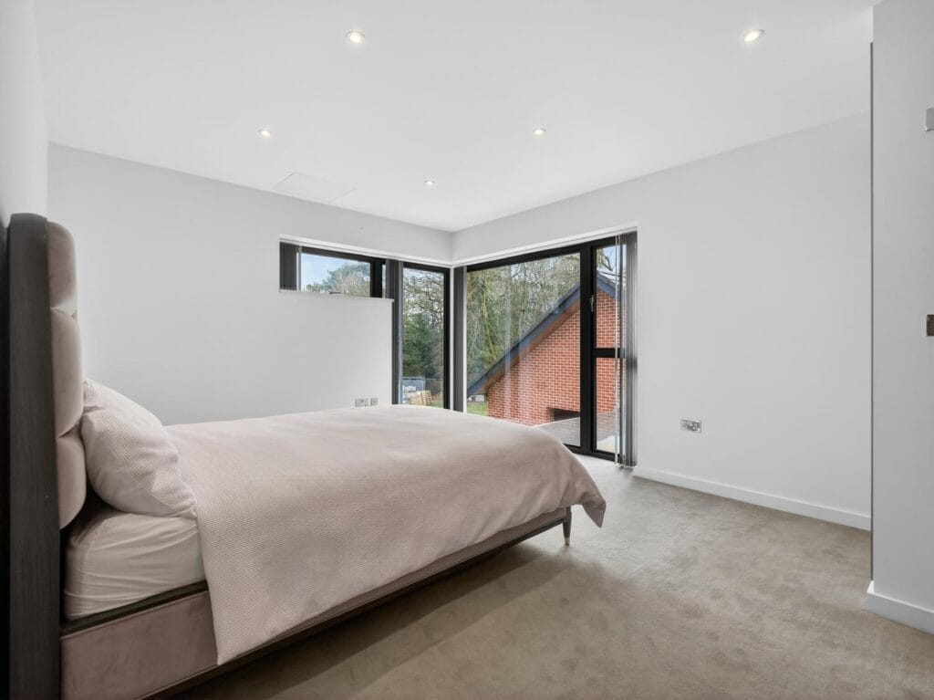 Modern double bedroom with corner windows providing natural light and views across the garden.