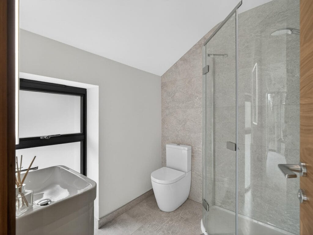Contemporary ensuite shower room with glass shower enclosure, modern tiling and frosted window for natural light.