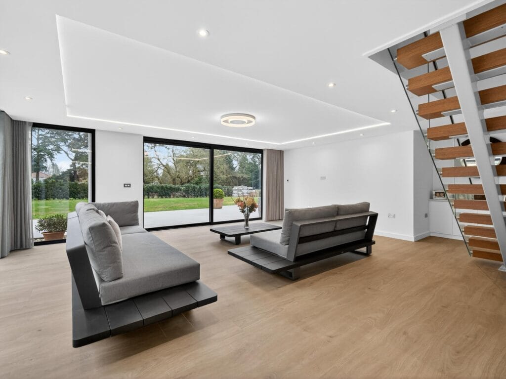 Modern open-plan living room with floor-to-ceiling sliding doors, garden views and contemporary floating staircase.