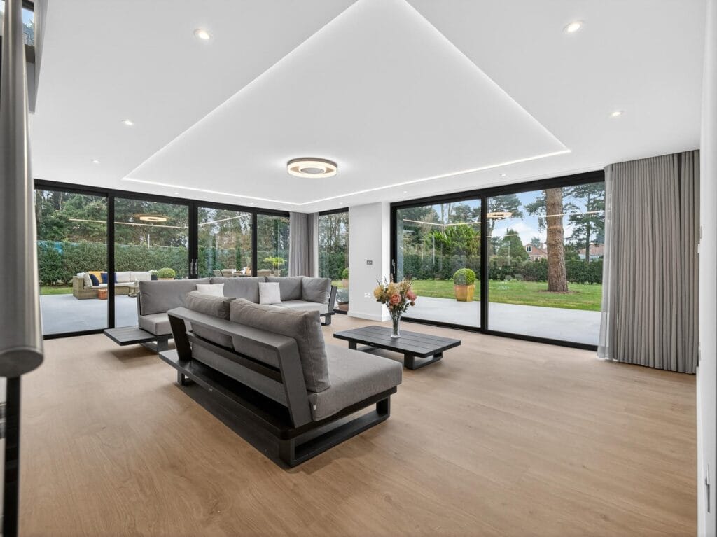 Luxury contemporary living room with wraparound floor-to-ceiling glass doors and views across the garden patio.