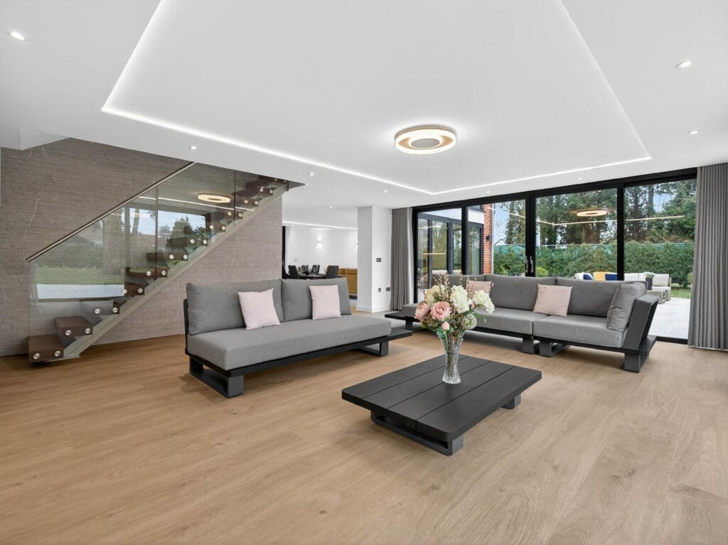 Contemporary living room with floating staircase, glass balustrade, floor-to-ceiling sliding doors and garden views.