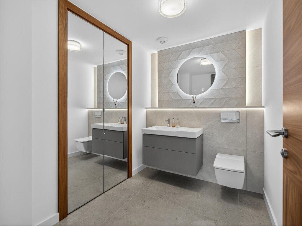 Contemporary bathroom with floating vanity, illuminated round mirror, wall-hung WC and modern tiled finish.