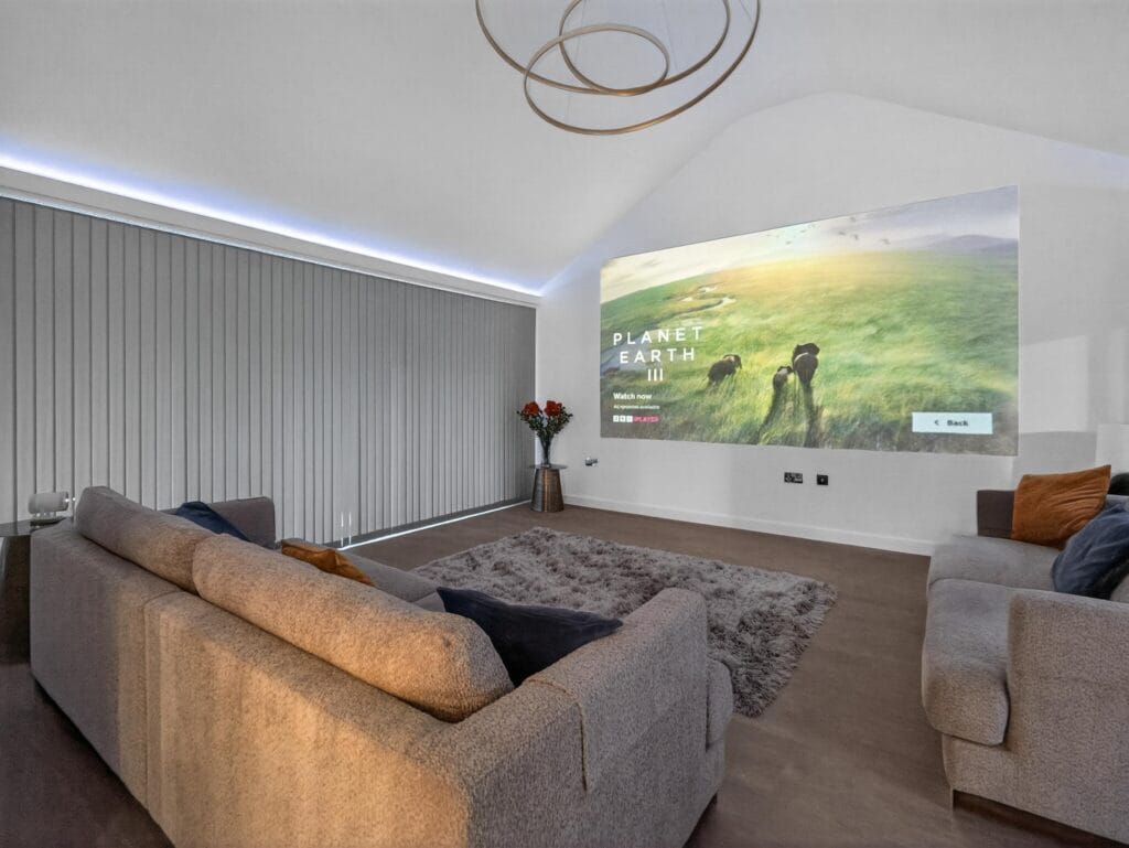 Luxury home cinema media lounge with projector screen, vaulted ceiling, soft lighting and comfortable seating.