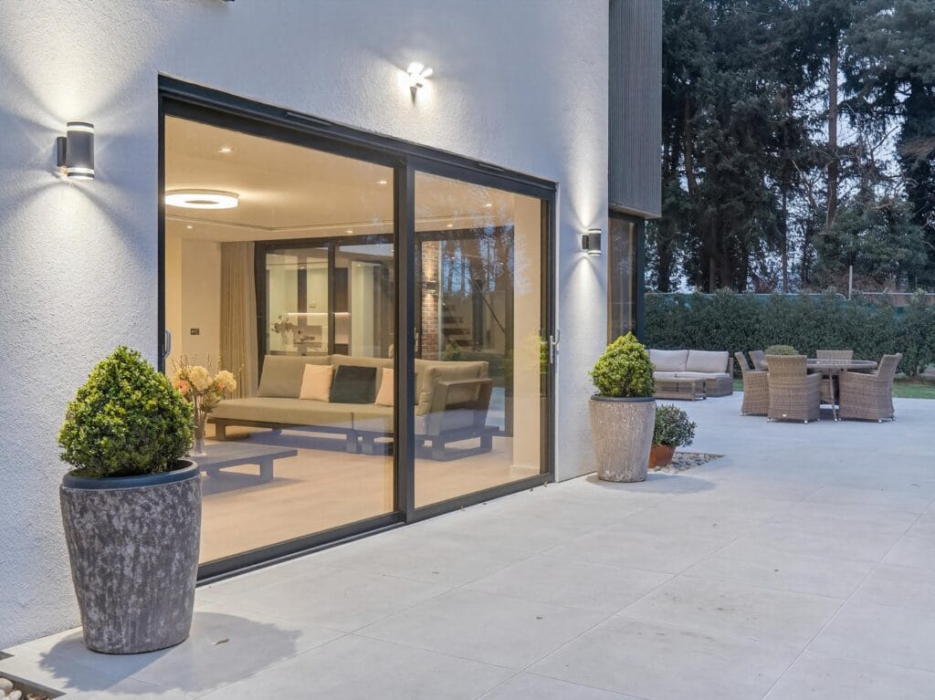 Modern luxury home patio with large sliding glass doors opening to a contemporary living space and outdoor seating area.