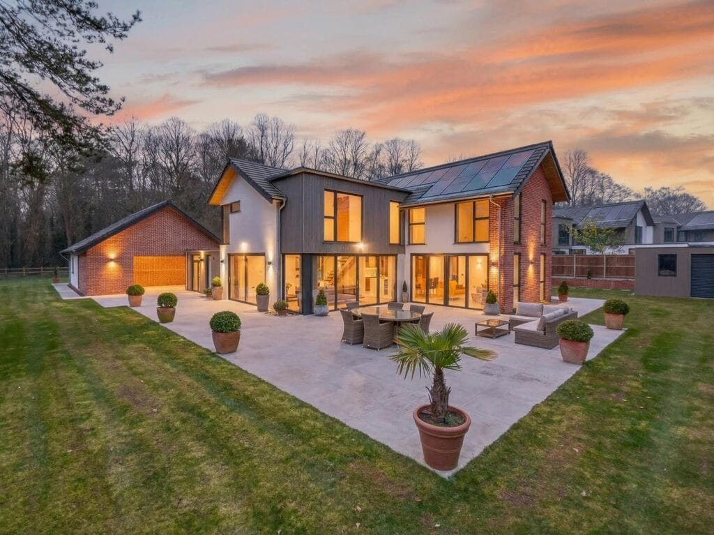 Contemporary luxury home rear elevation at dusk with large patio terrace, garden and floor-to-ceiling glazing.