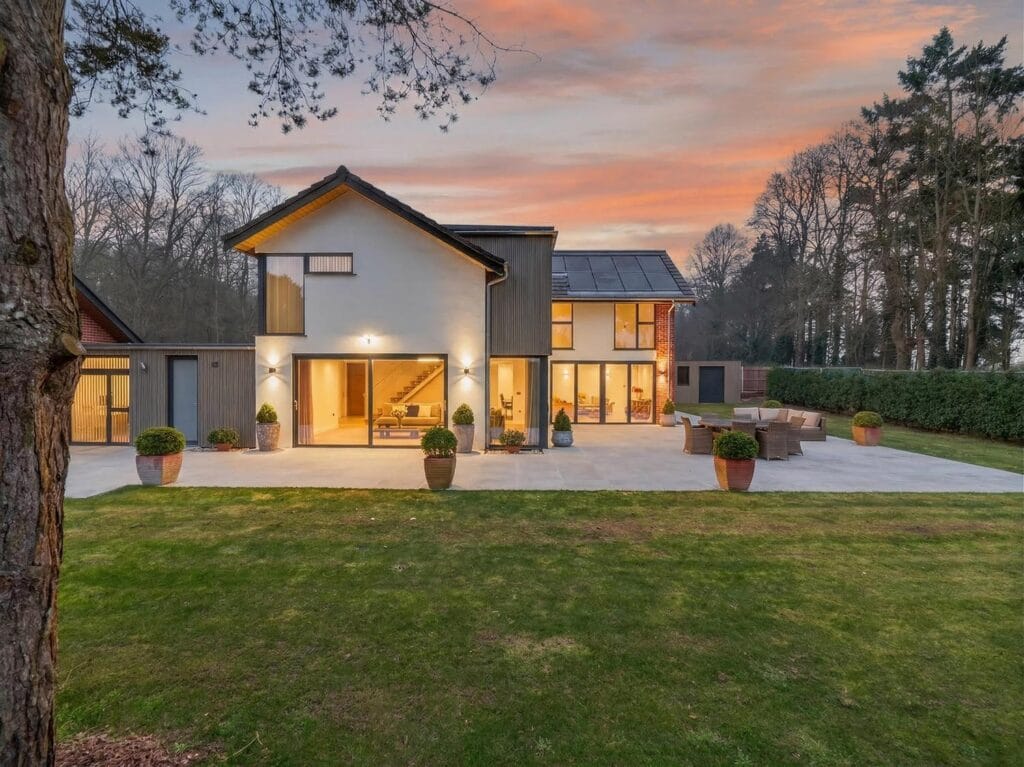 Modern architect-designed luxury home with large patio terrace and landscaped garden photographed at sunset.