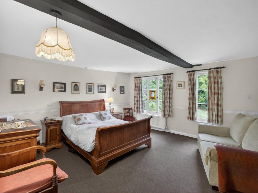 Bedroom at The Priory Suffolk with substantial blackened ceiling beam, dual aspect windows and small armorial stained glass panel