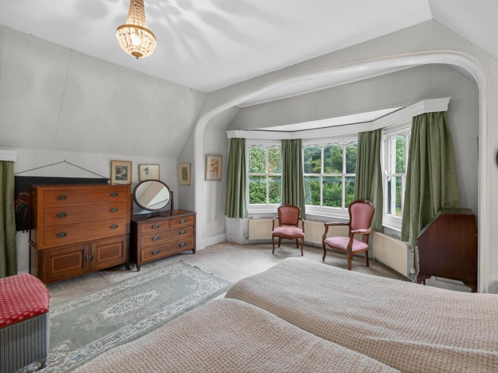 Principal bedroom at The Priory Suffolk shown from the bed end with curved bay window and arched architrave