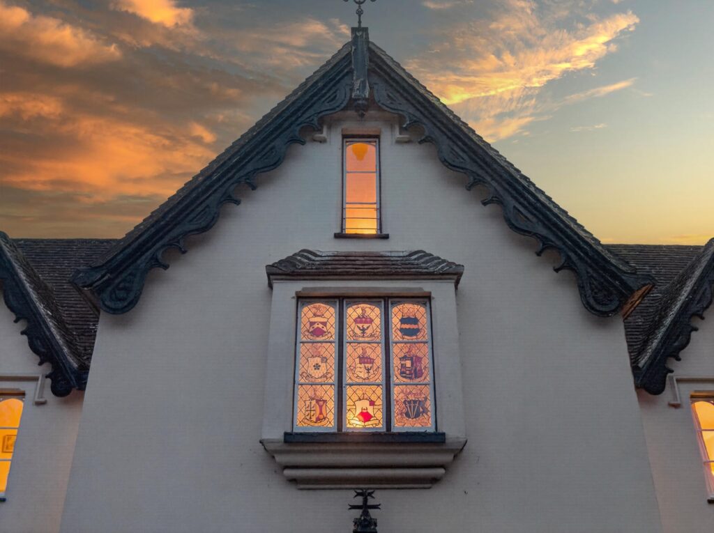 Heraldic stained glass oriel window of The Priory Suffolk illuminated against a sunset sky