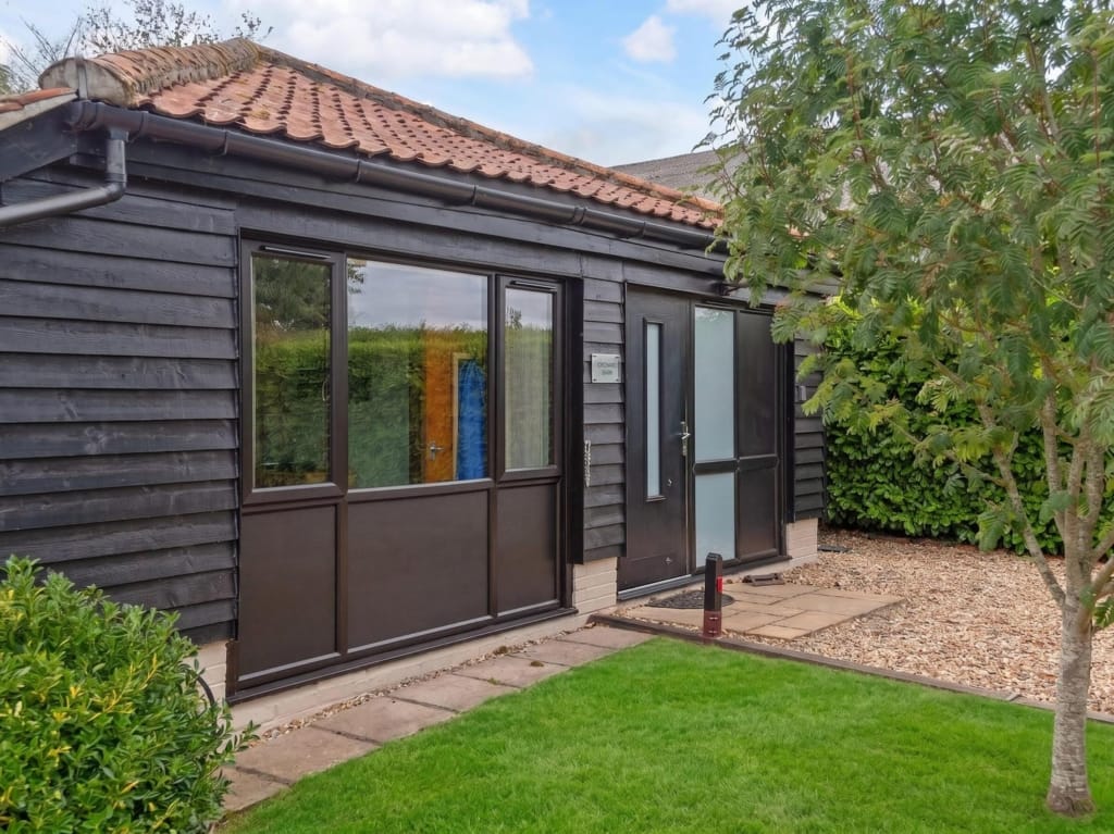 Orchard Barn exterior with dark timber cladding, glazed doors, pantile roof, and lawned garden, Sisland, Norfolk