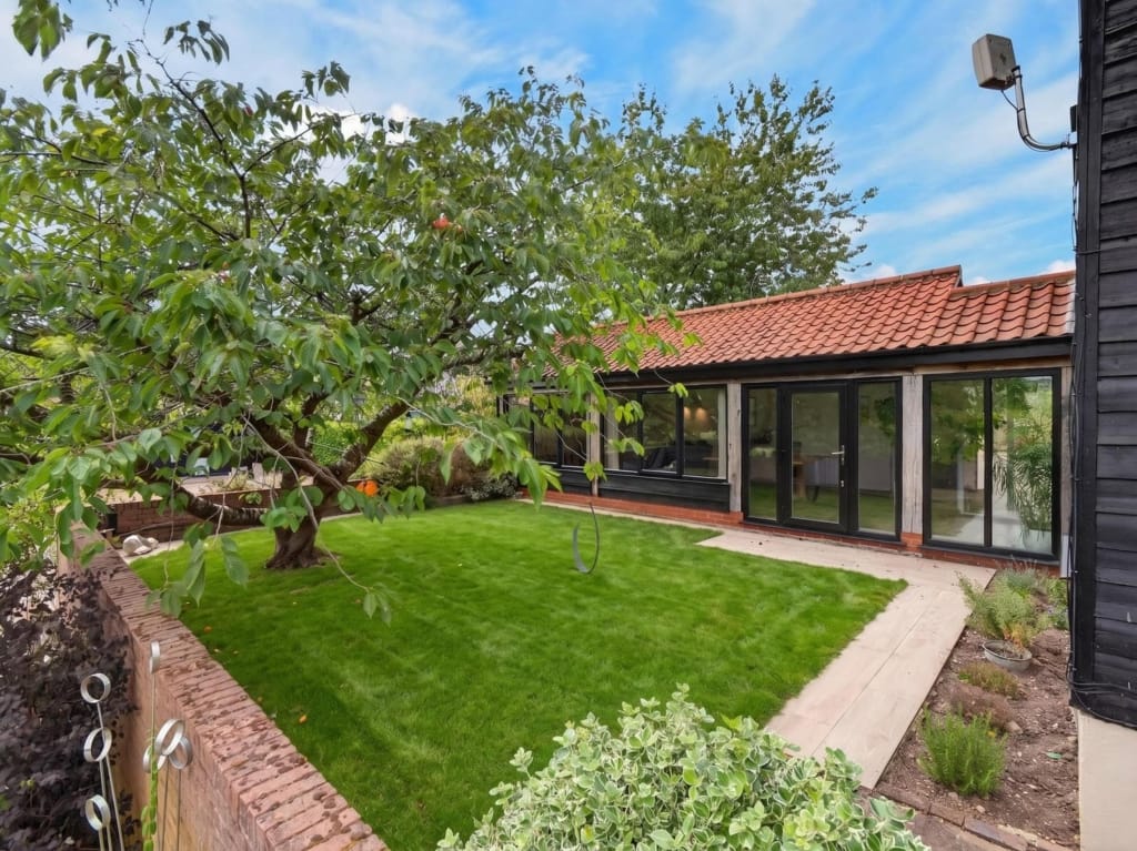Rear garden at The Tithe Barn Sisland with lawn, mature fruit tree, and glazed bifold doors to single-storey extension under pantile roof