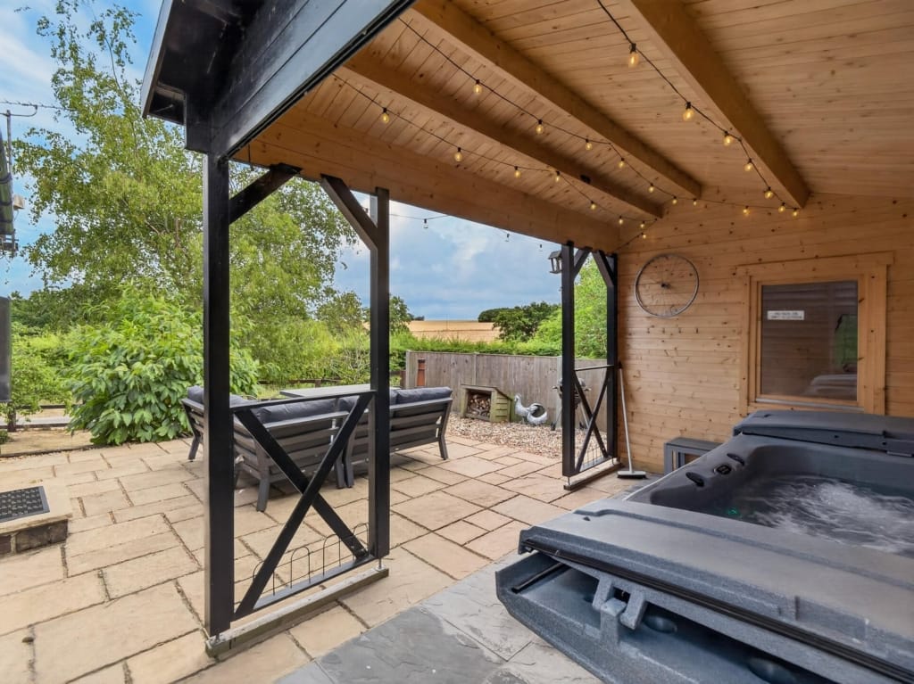 Covered outdoor entertaining area with hot tub, festoon lights, and paved terrace at The Tithe Barn, Sisland, Norfolk