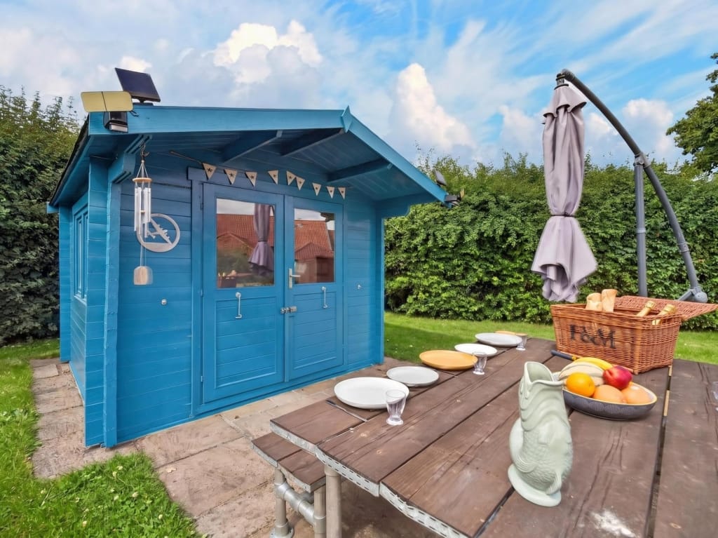 Garden summerhouse painted blue with outdoor dining table, picnic hamper and parasol, The Tithe Barn, Sisland, Norfolk