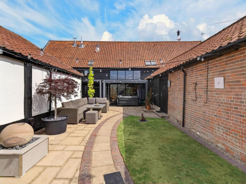 Courtyard at The Tithe Barn Sisland Norfolk showing sandstone paving outdoor sofa hot tub and red-pantile barn rooflines