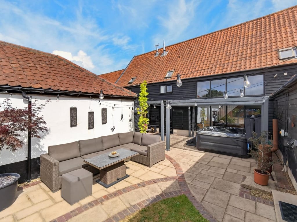Courtyard terrace at The Tithe Barn Sisland with rattan seating, hot tub, and festoon lights beneath pantile rooflines