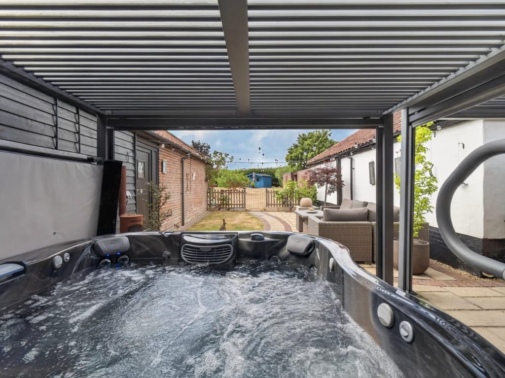 Hot tub under louvred pergola with courtyard seating and barn buildings beyond, The Tithe Barn, Sisland, Norfolk